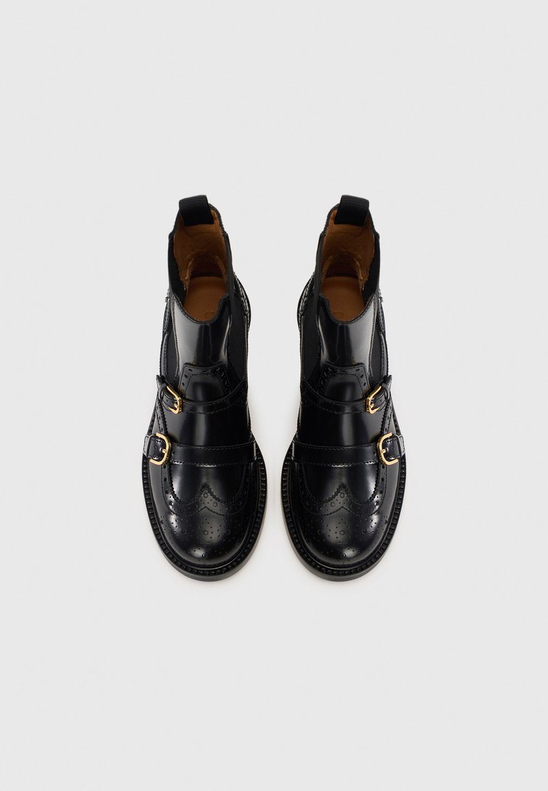 Stivaletti neri in pelle con dettagli brogue, accenti a doppia fibbia e pannelli elasticizzati. Texture liscia e design a punta tonda.