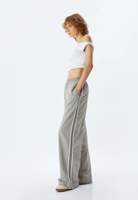 Pantalon large gris avec des rayures noires, taille élastique et poches latérales, associé à un top blanc court décolleté.