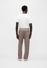 Καρό παντελόνι σε καφέ και κρεμ με ρίγες στο πλάι και τσέπες μπροστά και πίσω. Συνδυάζεται με απλό λευκό T-shirt.