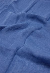 Miękka niebieska lniana tkanina z widoczną teksturą splotu i naturalnymi fałdami, tworzącymi delikatne fale na powierzchni.