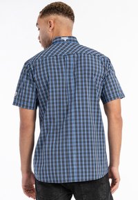 Short-sleeve shirt in a blue and black checkered pattern. Fabric is woven with a smooth texture. Features a low collar and stitched tag.