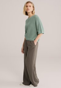 Pull en tricot vert menthe avec une coupe ample et des manches courtes, associé à un pantalon gris à jambes larges en tissu doux et fluide.