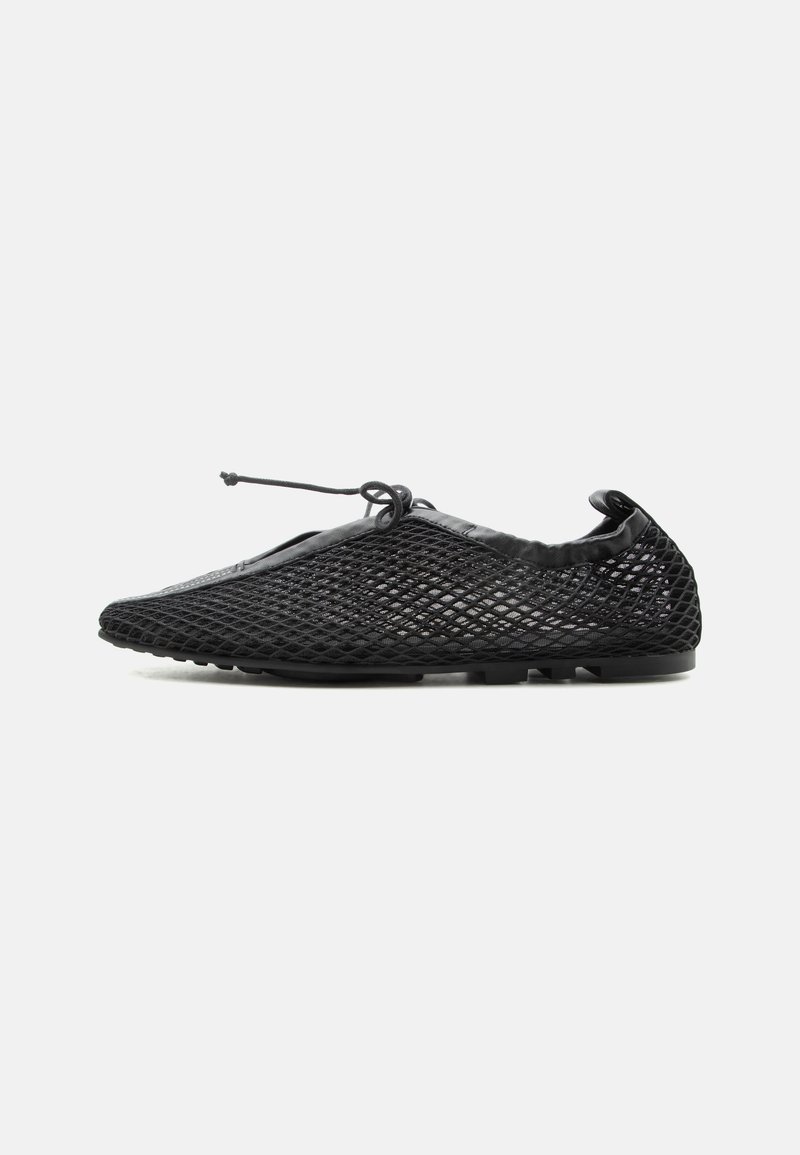 Chaussure slip-on en mesh noir avec une semelle fine et un lacet ajustable noué sur le dessus, présentée de profil sur fond blanc.