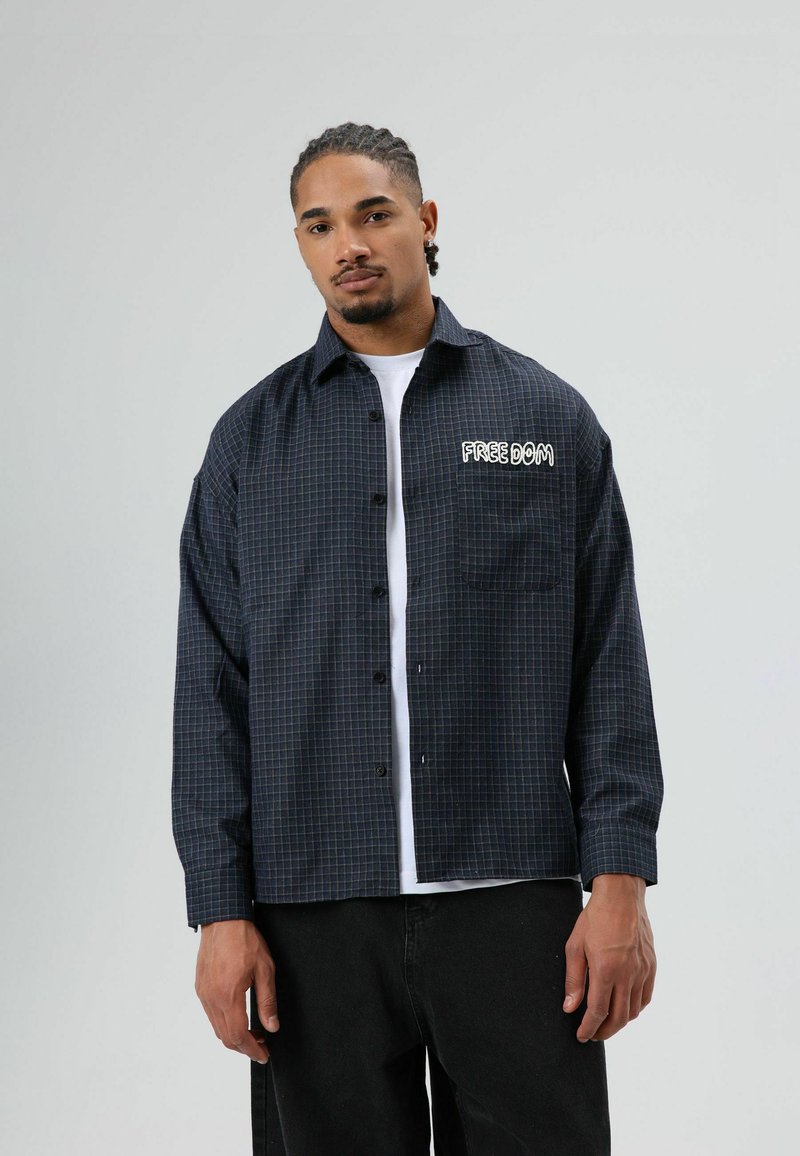 Zwart en marineblauw ruitjes overhemd met knopen, een borstzak en "FREEDOM" geborduurd in het wit. Lange mouwen en een comfortabele pasvorm.