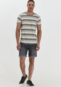 Camisa de manga corta a rayas en beige y gris, combinada con unos pantalones cortos de mezclilla oscuros. Zapatillas negras completan el conjunto. Diseño simple y casual.