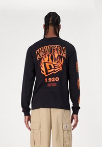 Schwarzes Langarmshirt mit orangefarbenem Flammendesign und dem Text "NEW ERA 1920" auf dem Rücken und den Ärmeln. Hergestellt aus weichem, atmungsaktivem Stoff.