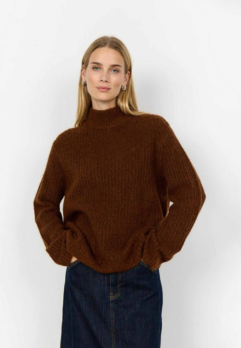 Brun, texturerad stickad tröja med hög krage och lös passform. Matchad med en mörk jeanskjol. Tyget verkar mjukt och varmt.