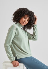 Mint green pullover with a zippered neckline, long sleeves, and side slits. Made of smooth material with subtle texture and elastic cuffs.