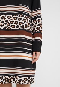 Black dress featuring horizontal stripes in brown, white, and cream, with a leopard print band near the hem. Soft fabric, loose fit.