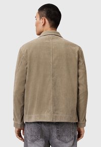 Beige kordjacka med en avslappnad passform, synlig ribbad textur och en klassisk krage. Bakvy visar skräddarsydda sömmar och knappade manschetter.