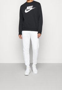 Svart sweatshirt med vitt Nike-logotyp, kombinerad med vita sweatpants och vita sneakers. Avslappnad outfit med en enkel och ren design.