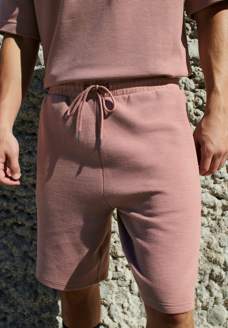 Lyserøde ribbede shorts med elastisk talje, justerbar snor og en afslappet pasform med sidelommer.