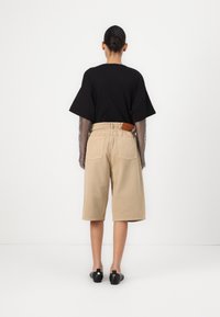 Černé oversized tričko s krátkým rukávem, béžové cargo šortky s vysokým pasem, kožená nášivka na zadní straně a černé ploché boty.