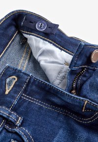 Mørkeblå denimjeans med et let stofforing indeni, gyldne stikninger og en linningknap med logo. Lynlås lukning.