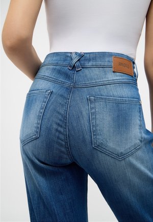 Jeans de denim azul con un diseño de cintura media, dos bolsillos traseros y un parche de cuero marrón de la marca en la cinturilla.
