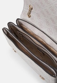 Gestructureerde lichtbeige handtas met een gemusterde buitenkant, drie compartimenten binnenin en een gouden kettingaccent. Merkenlogo zichtbaar op de voering.