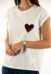 Camiseta blanca de manga corta hecha de algodón, con un estampado de corazón burdeos en el pecho y la palabra "COEUR" debajo.