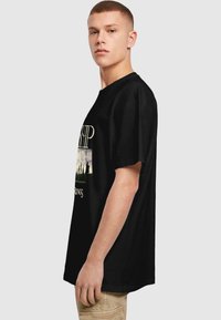 T-shirt en coton noir avec une coupe décontractée, featuring un design graphique sur le devant avec des accents blancs et verts. Manches courtes et col rond.