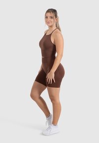 Bruine sport-bh en bijpassende shortset, gemaakt van een gladde stof. Kenmerkt zich door een gevormd ontwerp met dunne bandjes en een hoge taille. Witte sneakers.