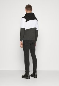 Grijze, zwarte en witte kleur geblokte hoodie met een trekkkoord capuchon, gecombineerd met zwarte slim-fit jeans en zwarte enkellaarzen. Zachte textuur.