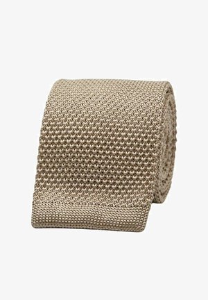 Beige punottu vyö, jossa on tekstuuri ja uritettu kuvio. Materiaali on pehmeä ja joustava, rullattu siististi esillepanoksi.