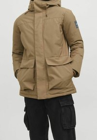 Mörk huvad jacka med blixtlås, två stora framfickor och en slät, texturerad yta. Har en logotyp på vänster ärm.