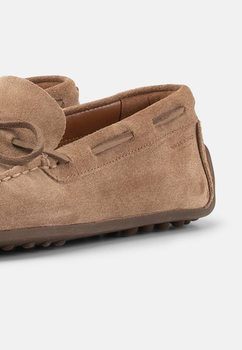 Lichtbruine suède mocassin met een afgeronde neus, veterdetail rondom de bovenkant en een rubberen zool met pebbelprofiel.