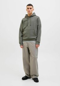 Olive green hoodie with drawstring, kangaroo pocket; paired with light beige wide-leg pants and black shoes. Minimalist design, soft texture.