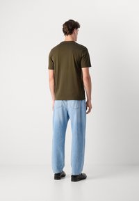 T-shirt en coton vert olive à col rond, assorti à un jean en denim bleu clair ample et des chaussures noires, vu de dos.