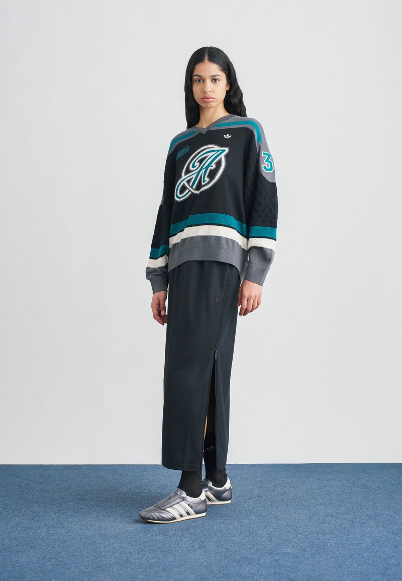 Pull noir style hockey avec accents turquoise et gris, associé à une longue jupe noire dotée d'une fermeture éclair latérale. Des chaussures de sport argentées complètent la tenue.
