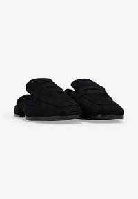 Mules negros de ante suaves y sin ataduras. Presentan una punta redonda, costuras decorativas y un tacón bajo sólido con una base lisa.