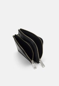 Portefeuille en cuir noir avec deux compartiments zippés, doté de quincaillerie en argent et de coutures contrastantes dorées le long des zips.