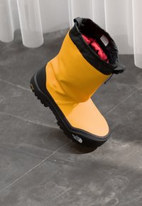 Stivale giallo impermeabile con bordo superiore nero, tomaia strutturata e suola nera caratterizzata da una battistrada decorata per una migliore aderenza. Fodera interna rossa.