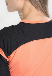 Maglietta sportiva con una parte superiore nera strutturata e una parte inferiore di un solido colore corallo, con scollo arrotondato e cuciture a contrasto.