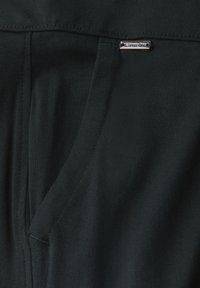 Svart stretchtyg med en slät textur har en sidoficka och en diskret metallisk logotagg. Enkel design och skräddarsydd passform.