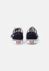 Marineblaue Wildleder-Schnürschuhe mit weißen Gummisohlen, kontrastierenden Nähten und rotem Logo-Tag an der Ferse. Klassisches Skate-Schuhdesign.