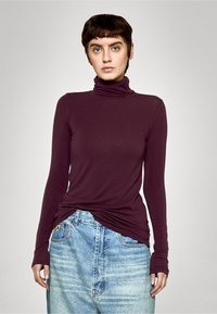 Burgunderfarget langermet turtleneck-topp laget av mykt stoff, kombinert med en lysvasket, slitt denimskjørt. Har smal passform og omslagsdesign.