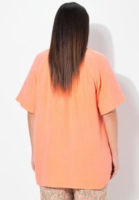 Orangenes Kurzarmoberteil aus strukturiertem Stoff, lockere Passform und abgerundetem Saum, kombiniert mit gemusterten Hosen mit floralen Designs.