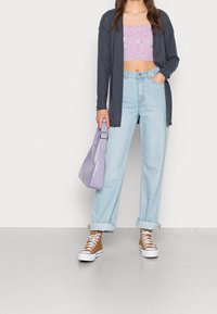 Lässiges Outfit mit einer dunklen Strickjacke, hellblauen High-Waist-Jeans, einem lavendelfarbenen Cropped-Top und braunen High-Top-Sneakern. Eine lavendelfarbene Tasche ist ebenfalls dabei.