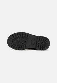 Suela de goma negra con un patrón de surcos profundo, que presenta tacos hexagonales y en forma de cruz para tracción y durabilidad. Construcción sólida.