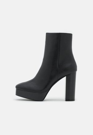 Schwarzer Leder-Stiefelette mit Plateau-Sohle und hohem Kloblockabsatz, Seitenansicht vor schlichtem hellem Hintergrund.