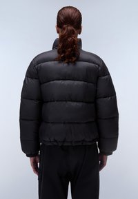 Zwarte pufferjack met een hoge kraag, geborduurd ontwerp en elastische manchetten. Heeft een cropped silhouet en een gladde, glanzende stoftextuur.