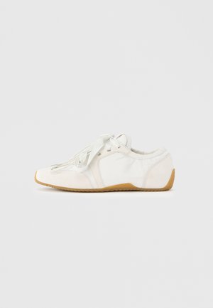 Valkoinen tennari, jossa pehmeä päällinen, vaaleat kengännauhat, pyöreä kärki ja kumipohja. Sileä pinta ja kaarevat muotoilulinjat.