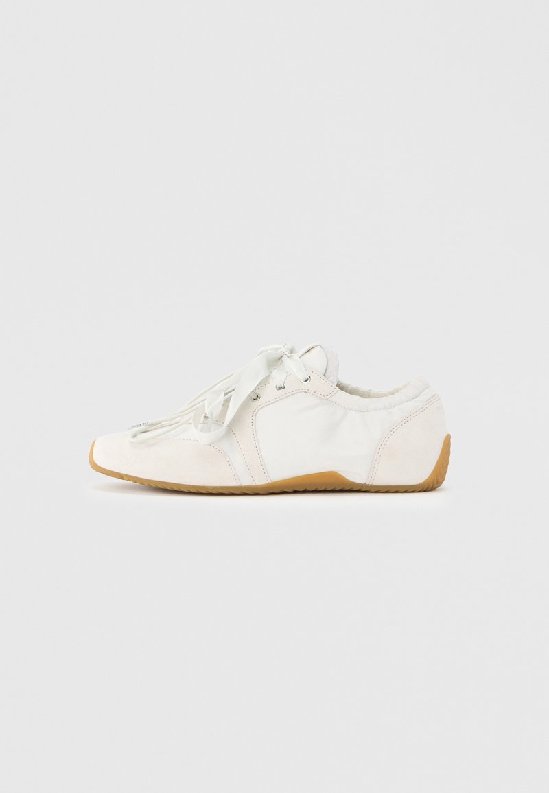 Hvid sneaker med blødt overmateriale, lys snøring, rundet snude og sål af gummi. Glat tekstur med buede designlinjer.