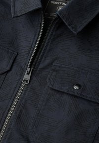 Giacca blu navy con zip, caratterizzata da un motivo testurizzato sottile, due tasche frontali con chiusura a scatto e una robusta zip in metallo.