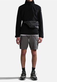 Giacca impermeabile nera con colletto alto, pantaloni cargo grigi e sneakers grigio/verde. Include una borsa a vita grigia. Tessuto testurizzato.