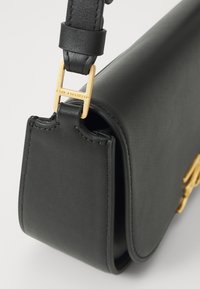 Black leather handbag with a smooth texture, featuring gold hardware and a distinctive clasp with the brand name engraved.