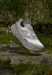 Hellgrauer Laufschuh mit atmungsaktivem Mesh-Obermaterial, Schnürverschluss, gepolstertem Kragen und robustem Außensohlenprofil mit gelben Profilierungen.