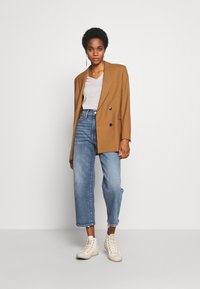 Brūns divrindu žakets, pelēks V veida kakla T-krekls, gaiši zili augsto vidukļa džinsi ar saplēstām malām un bēšas augstās čības.