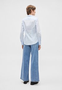 Svetlomodrá košeľa s gombíkmi a dlhými rukávmi, kombinovaná s širokými riflemi. Materiál je hladký s mierne lesklým povrchom.